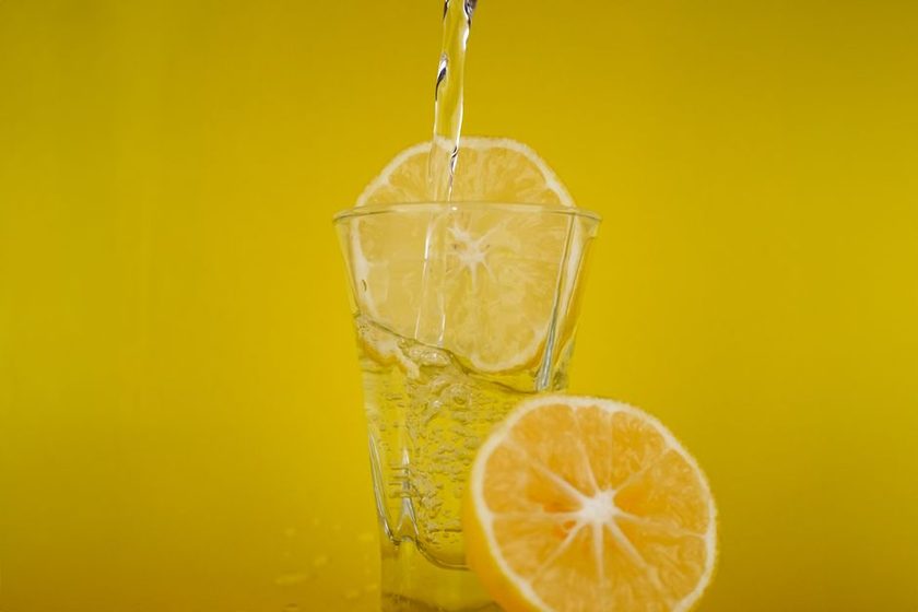 A glass of water with lemon and mint beside a bowl of fruit